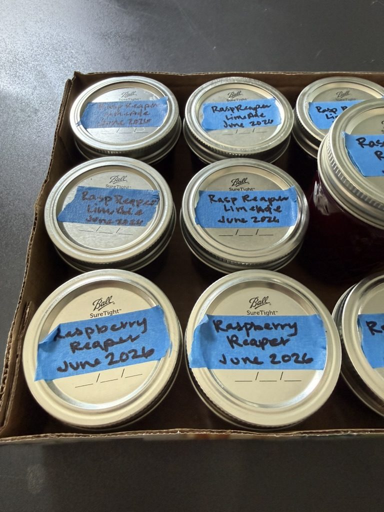 A box of jars labeled Raspberry Reaper and Rasp Reaper Limeade